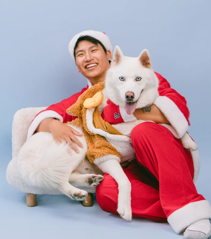 Jace in a Santa suit, laughing, holding his white husky Whitley.