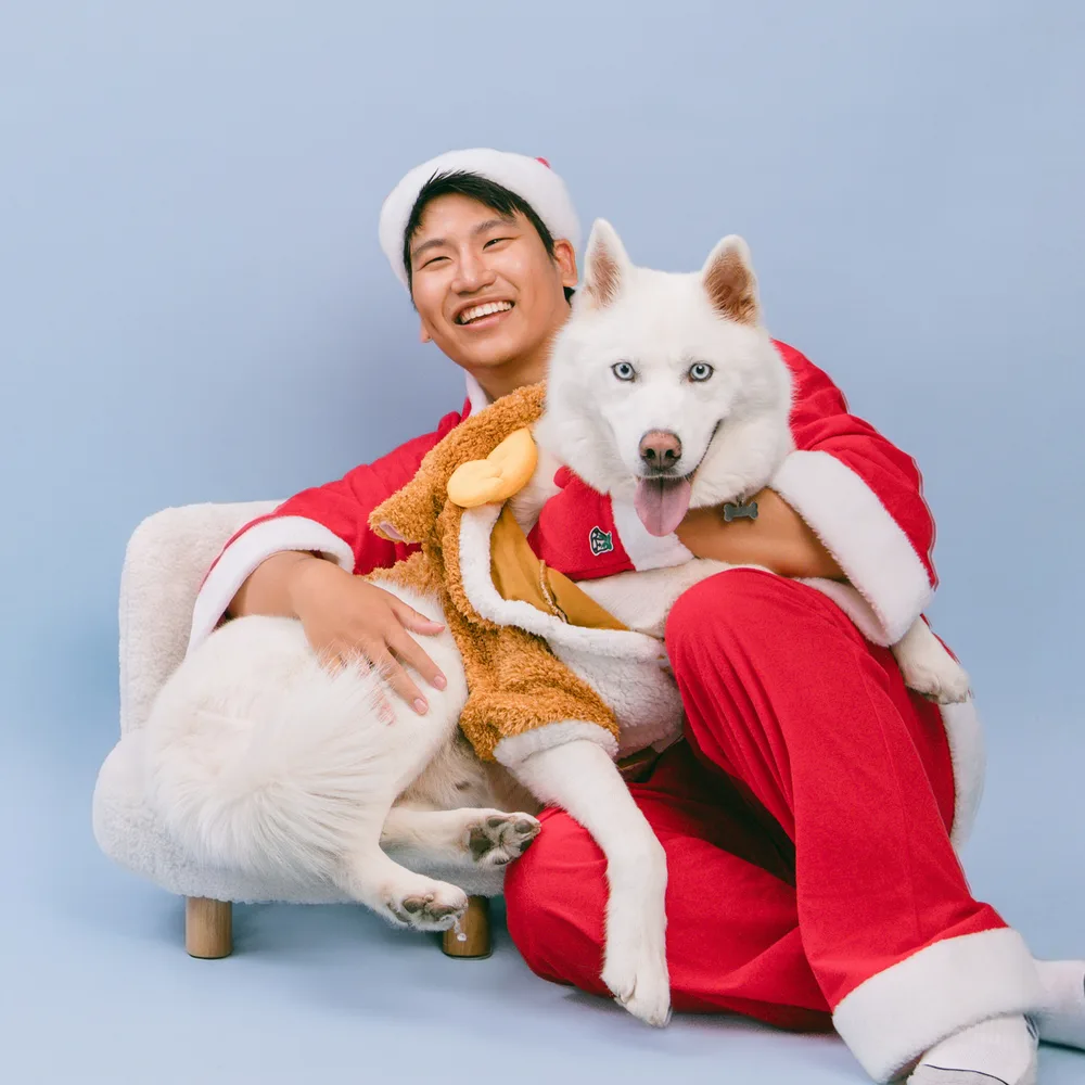 Jace in a Santa suit, laughing, holding his white husky Whitley.